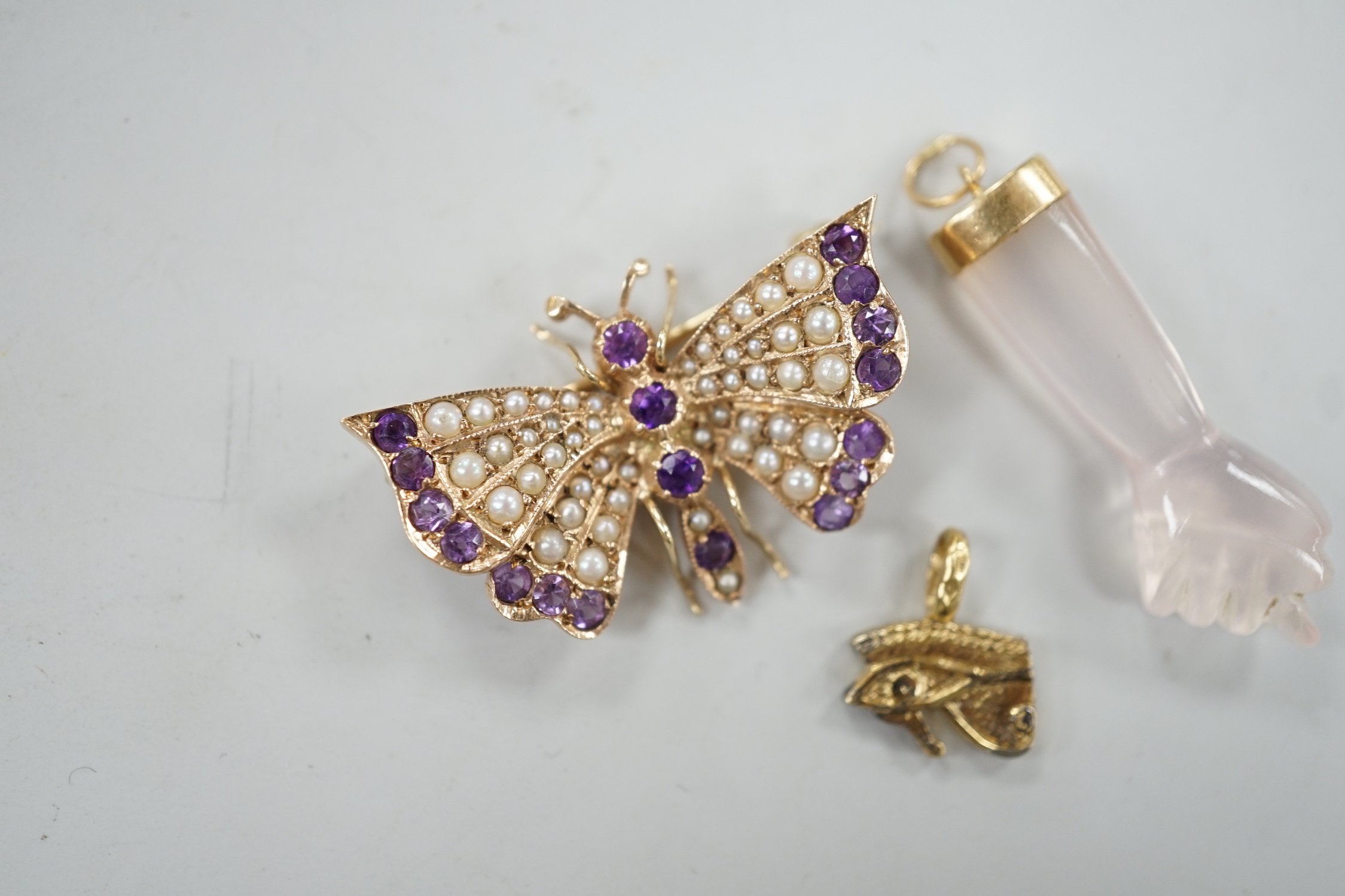 A modern 9ct gold, amethyst and seed pearl cluster set butterfly brooch, width 32mm, together with two charms including arm and fist.